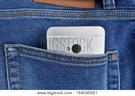 Silver aluminum smartphone placed at the male stitched blue jean's backpocket