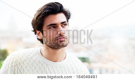 Beautiful model Italian man. A charming young man outdoors alone, looking to one side with an expression slightly happy and satisfied. Much space at the side for the insertion of any customization.
