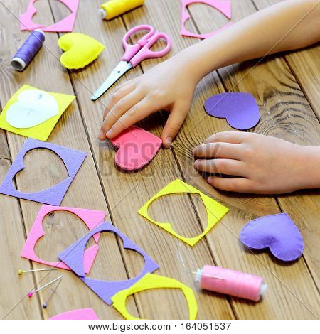 Child made hearts out of felt. Children's hands on the table. Handmade Valentines day heart gifts, crafts materials and tools on a wooden table. Valentine's day craft project