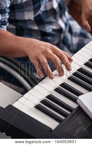 Enjoying every moment. Young devoted incapacitated man in a wheelchair experiencing new hobby of playing piano while spending his leisure time at home