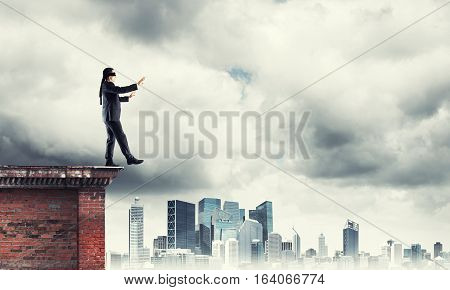 Businessman with blindfolder on eyes walking on building top