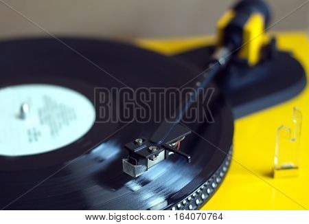 Vinyl LP record with red label sound reproduction on vintage turntable record player with yellow case. Horizontal photo closeup