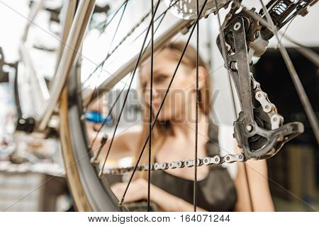 Fixing of the mountain bicycle. Concentrated watchful female technician standing in the garage near the mountain bicycle and working while repairing it