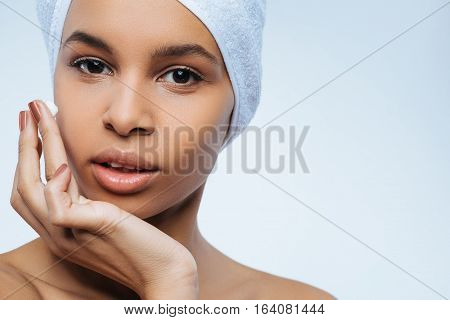 Skin care beauty products. Good looking nice pleasant woman applying facial cream and looking at you while wearing towel on her head