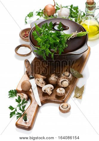 Cooking pot and uncooked ingredients for mushroom soup ( fresh brown champignon mushrooms olive oil spices) on a cutting wooden board isolated on white background.
