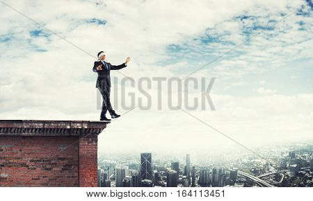 Businessman with blindfolder on eyes walking on building top