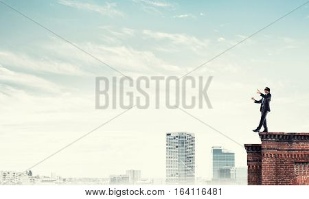 Businessman with blindfolder on eyes walking on building top