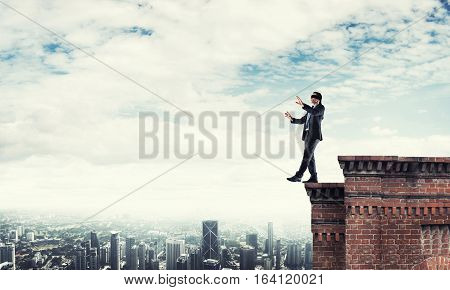 Businessman with blindfolder on eyes walking on building top