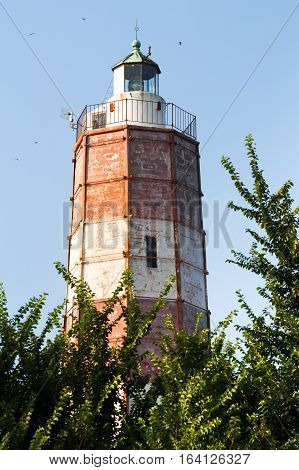 The Cape Shabla lighthouse the oldest on the Bulgarian Black Sea Coast Dobrich Province Bulgaria with its tall hexagonal tower painted red and white for aviation framed by green trees against a blue sky