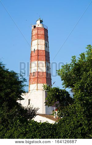 The Cape Shabla lighthouse the oldest on the Bulgarian Black Sea Coast Dobrich Province Bulgaria with its tall hexagonal tower painted red and white for aviation framed by green trees against a blue sky