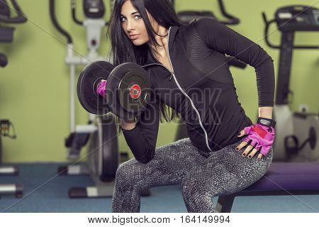 Attractive muscular young woman working out in a gym lifting weights