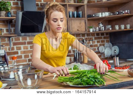 Attractive young woman holding green onions in kitchen