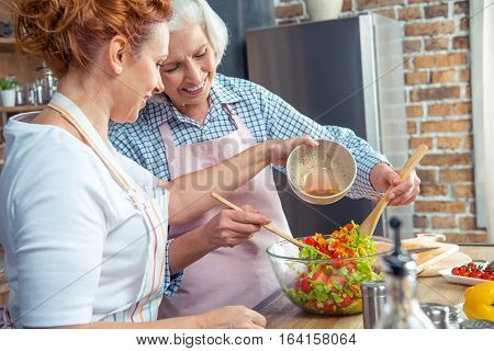 Two smiling women cooking vegetable salad together