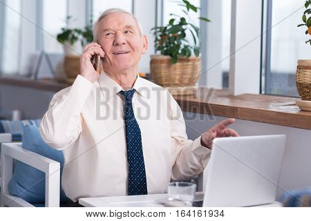 I can agree to that. Emotional handsome elderly man talking with his colleague on the phone while sitting in a restaurant and working on his laptop