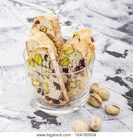 Crispy traditional delicious Italian biscotti cookies or kantuchchi with pistachios and dried cranberries in a glass on a marble background. selective focus