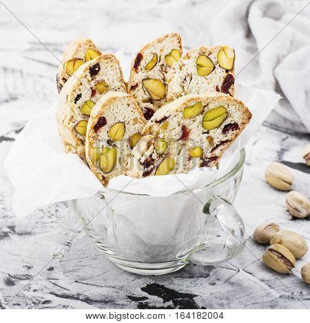 Crispy traditional delicious Italian biscotti cookies or kantuchchi with pistachios and dried cranberries in a glass on a marble background. selective focus