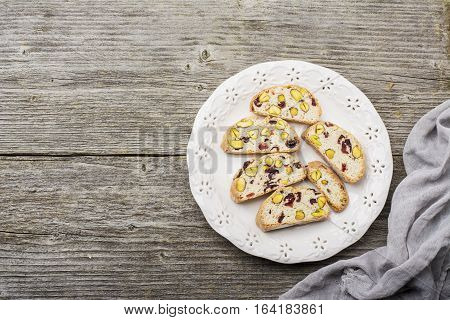 Crispy traditional delicious Italian biscotti cookies or kantuchchi with pistachios and dried cranberries in a glass on wooden background. selective