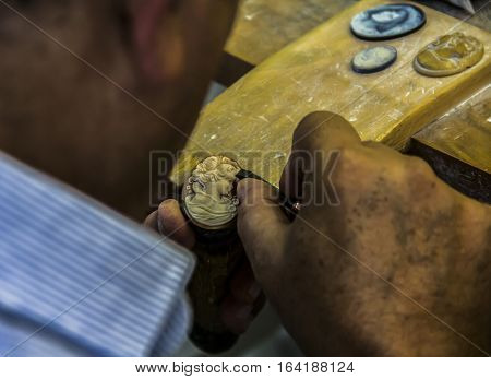 Pompeii, Italy:  close-up on his hands, a man uses a knife to carve a piece of seashell to make a cameo.