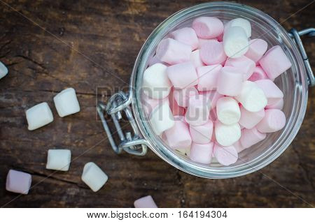 Pink and white mini marshmallows in a jar on an old rustic wooden table with space for text. Mini white and pink puffy marshmallows. Marshmallow concept. Copy space. Top view.