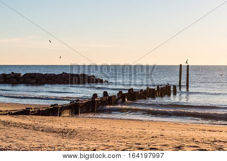 Dock pilings and rock jetty at sunrise at Buckroe Beach in Hampton, Virginia.