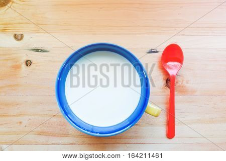 a cup of fresh milk and red spoon prepare for breakfast cereal on wooden table