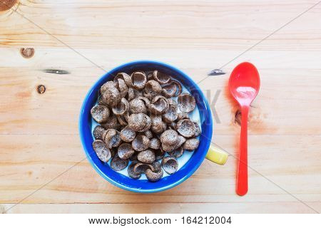 a cup of fresh milk mixed with cereal and red spoon prepare for breakfast on wooden table