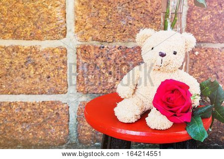 Adorable brown bear doll hold a red rose sitting on the round chair an idea of sending love