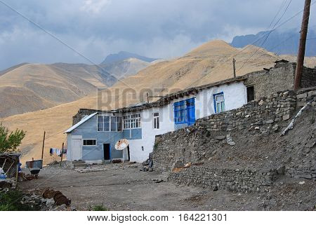 Xinaliq, Azerbaijan - August 23, 2014. Residential house in Xinaliq village, with linen put out to dry, satellite antenna and mountains in the background.