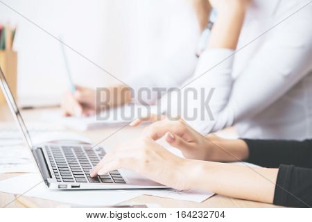 Close up of businesslady's hands using laptop computer placed on messy office desktop