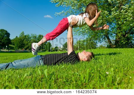 father and his daughter are playing on the green grass in a park