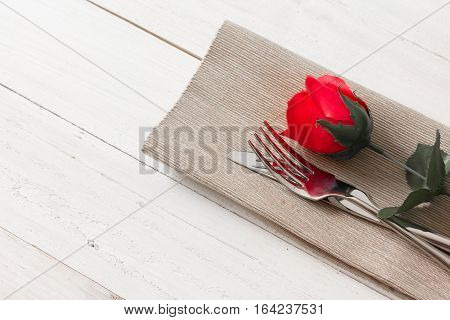 red rose with knife and fork on brown fabric with copy space