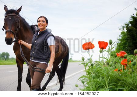 young woman is walking with her horse by the roadside