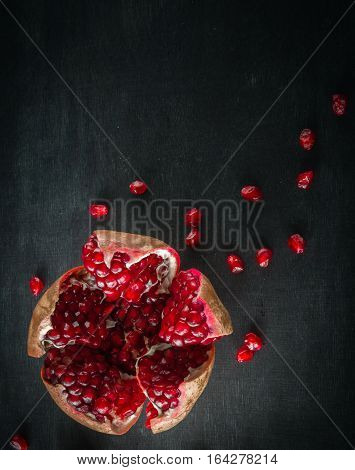 Red juicy ripe pomegranate grains on dark wooden background. View from above. Space for text.