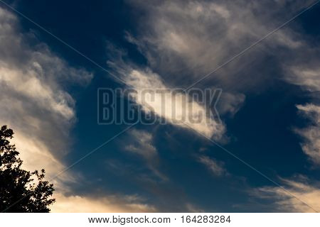 Dark blue sky with white airy clouds and a sun kissed corner.