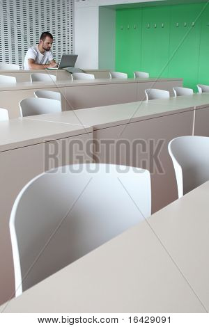 Junge männliche College-Studenten, die Arbeiten auf seinem Laptopcomputer in einem leeren Klassenzimmer