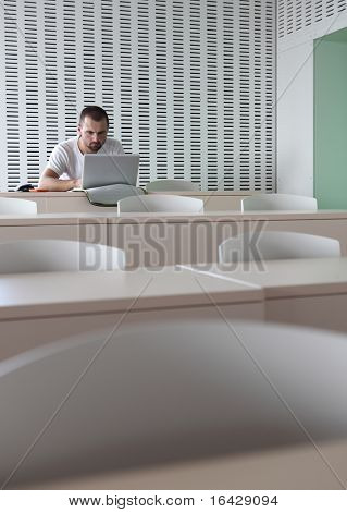 Junge männliche College-Studenten, die Arbeiten auf seinem Laptopcomputer in einem leeren Klassenzimmer