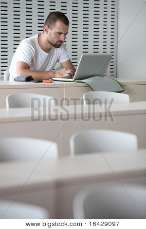 Junge männliche College-Studenten, die Arbeiten auf seinem Laptopcomputer in einem Klassenzimmer