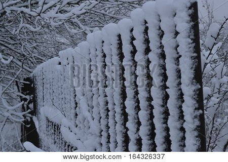 fence in winter park covered with heavy snow in frosty day