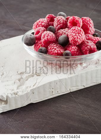 Frozen raspberries in a glass saucer. Frost on the berries. Dark background.