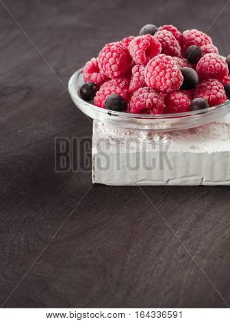 Frozen raspberries in a glass saucer. Frost on the berries. Dark background.