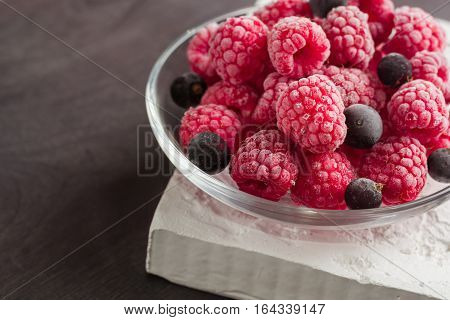 Frozen raspberries in a glass saucer. Frost on the berries. Dark background.