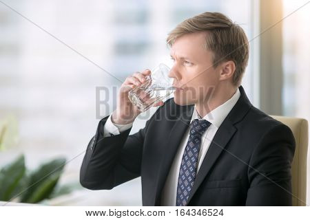 Young handsome businessman, drinking water, feeling tired foggy thinking and poor concentration, hot summer, feeling leaner and fitter, water supply in the office