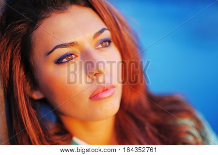 Portrait of young beautiful pensive woman with copper-brown hair in the bright rays of setting sun close up.