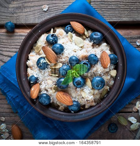 Oatmeal with blueberries, almonds, coconat and seeds at rustic wooden table. Flat lay.
