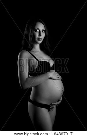Monochrome portrait of happy pregnant woman with hands over tummy. Black and white photo