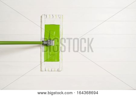 Cleaning floor with mop top view. Microfiber mop isolated on white wooden floor background. Home cleaning product concept photograph with copy space