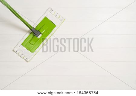 Cleaning floor with mop top view. Microfiber mop isolated on white wooden floor background. Home cleaning product concept photograph with copy space