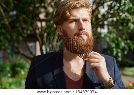 Red bearded hipster in summer time walking and comb out his beard.