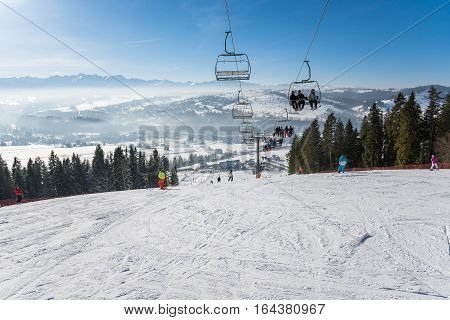 Czarna Gora Poland - December 30 2016: People go skiing on a sunny day with beautiful mountain view in the background.