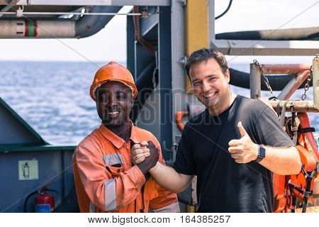 friendship of nations on board of ship/vessel. African seaman and European Chief Mate smiling and shaking hands on deck.